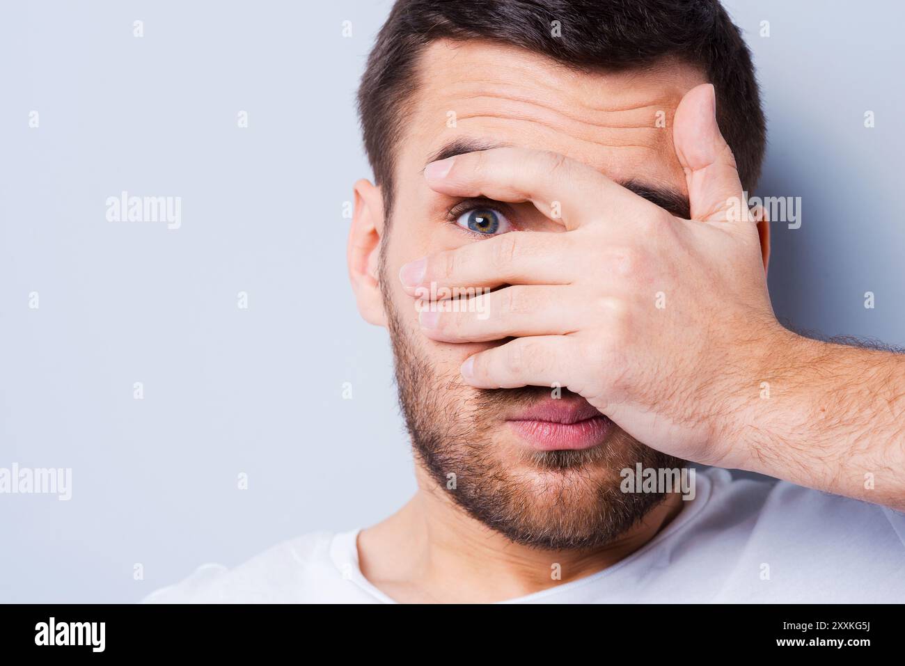 Shocked and terrified. Portrait of young man covering his face by hand ...