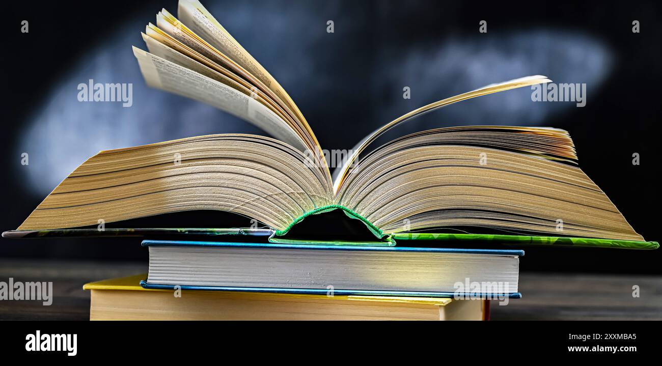 An open book lying on a stack of other books. Stock Photo