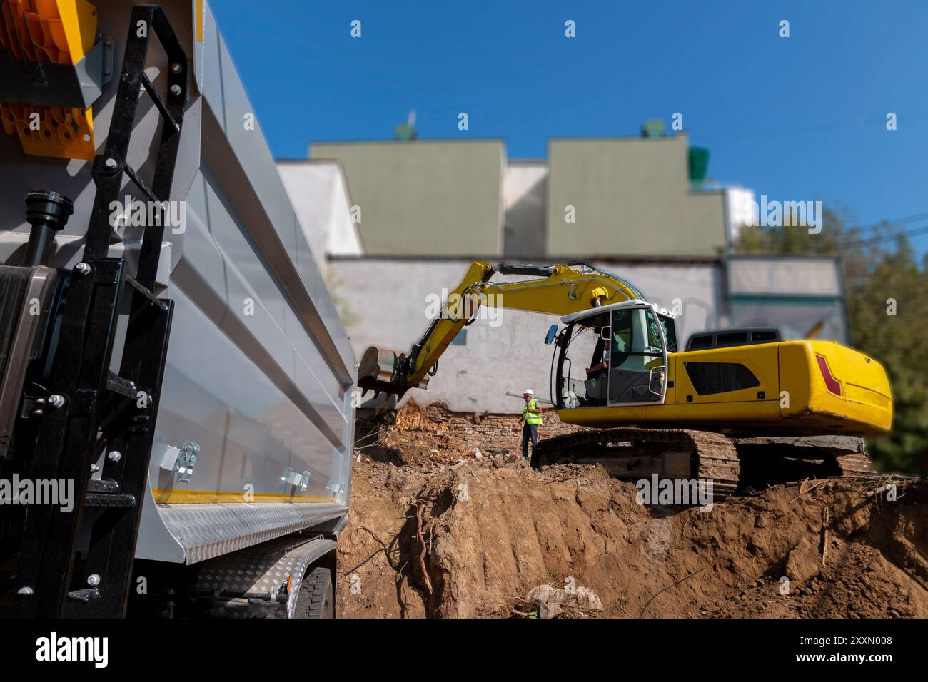 Big excavator is filling a dumper truck with soil at construction site, project in progress. Stock Photo