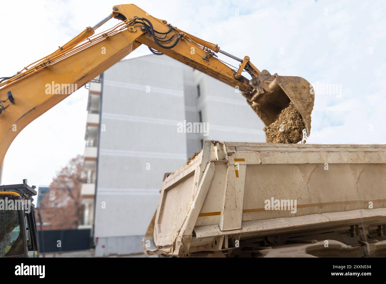 Big excavator is filling a dumper truck with soil at construction site, project in progress. Stock Photo