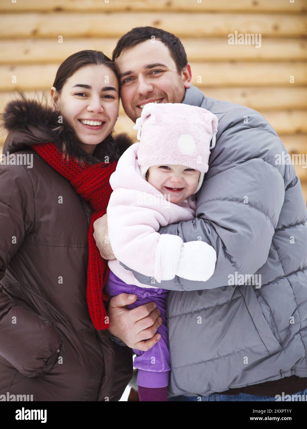 Beautiful family wearing warm clothes standing by wooden house in winter Stock Photo