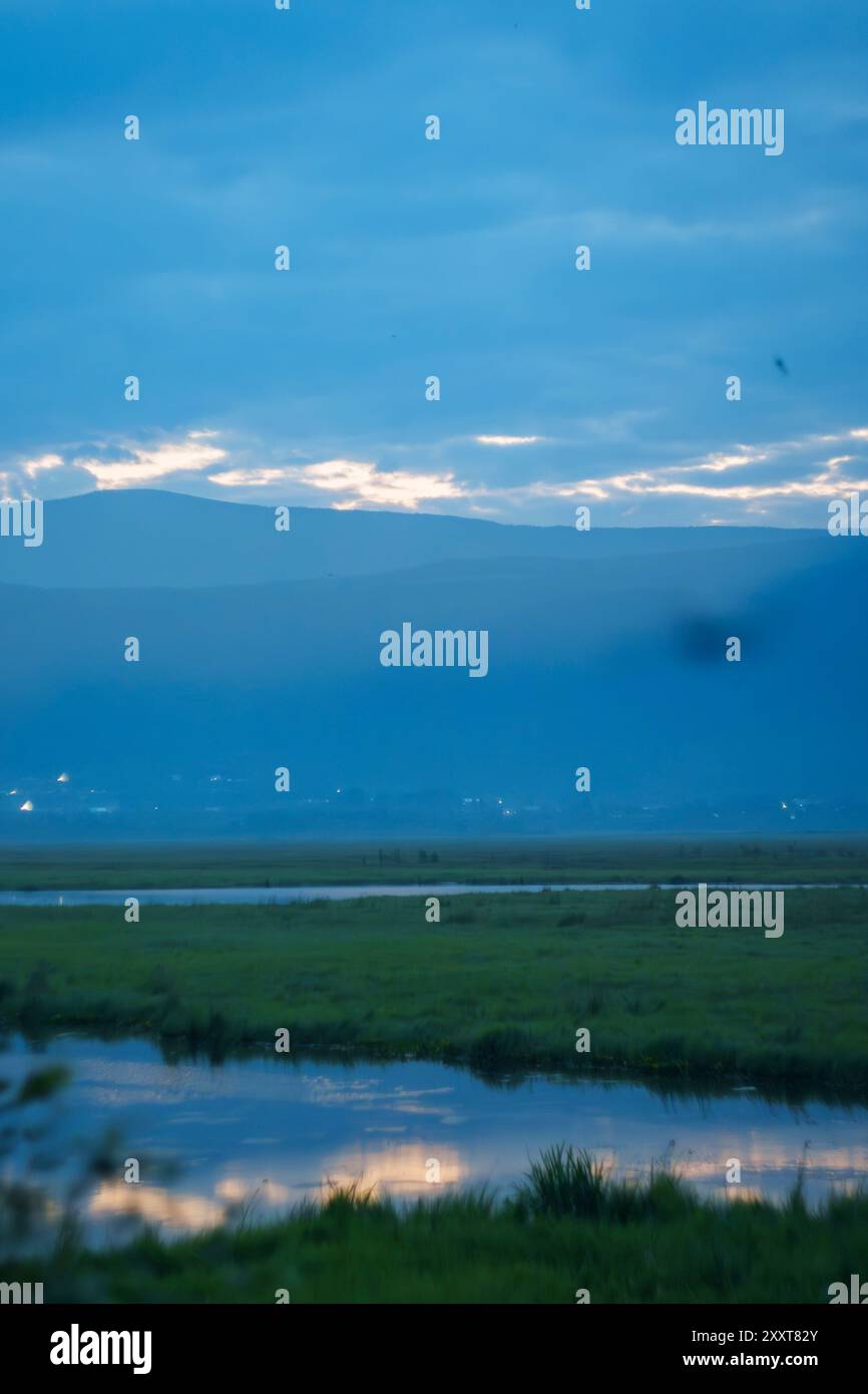A calm lake with misty mountains at dawn, surrounded by lush greenery ...