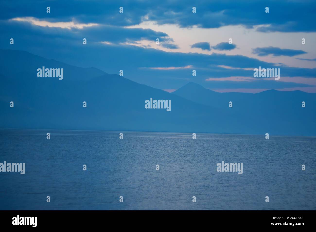 A calm lake with misty mountains at dawn, surrounded by lush greenery ...