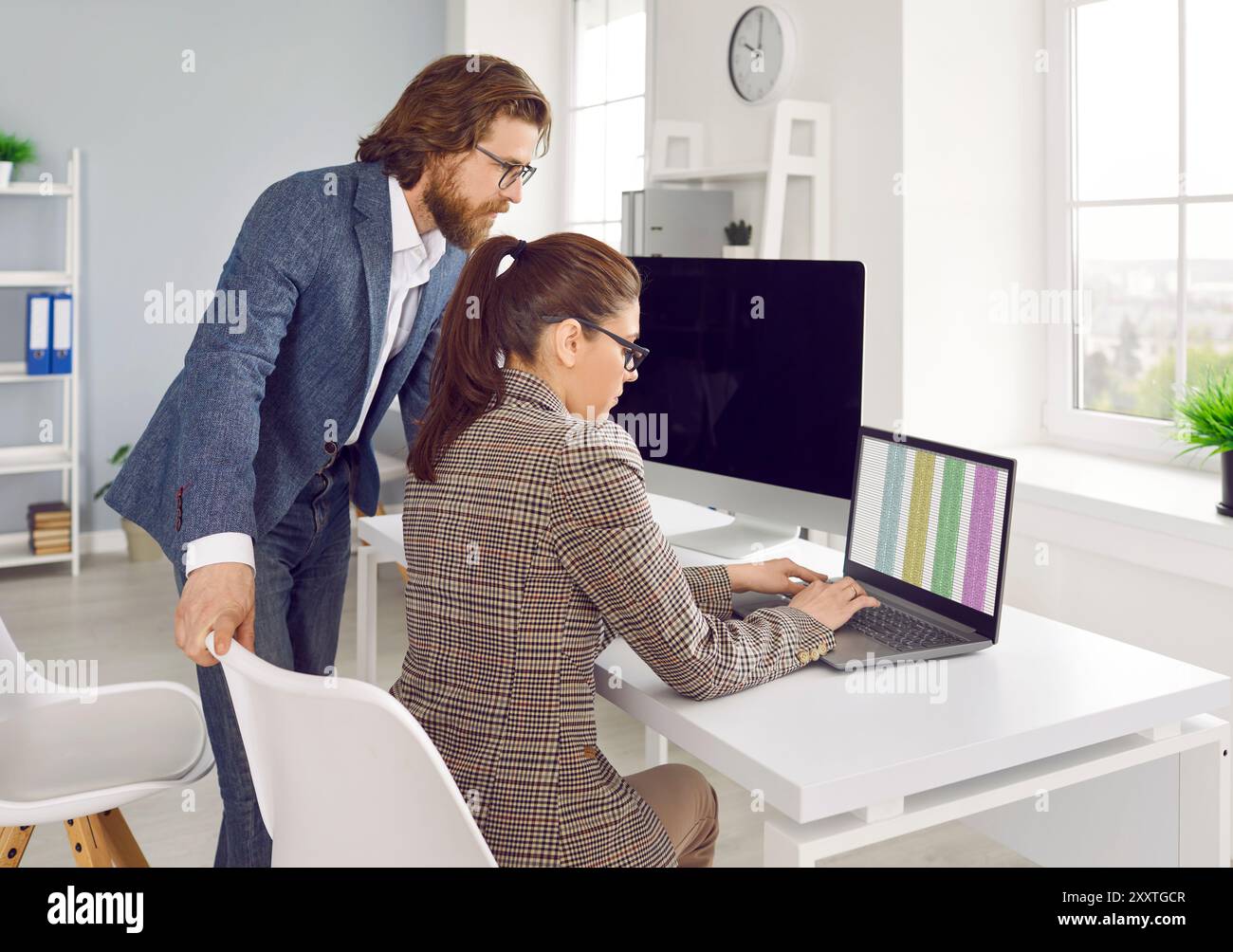 Two fellow accountants work together in office on financial report using laptop. Stock Photo