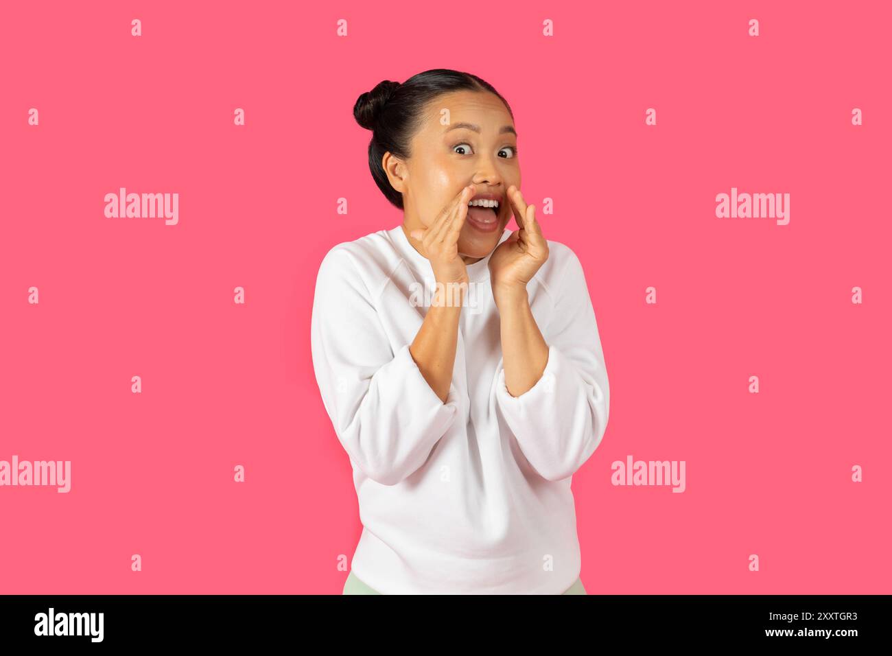Woman expressing excitement with joyful gestures against a pink background Stock Photo