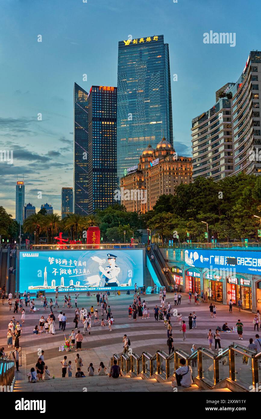 People walk in the Huacheng Square surrounded by modern high-rise buildings illuminated at dusk. Guangzhou, Guangdong Province, China. Stock Photo