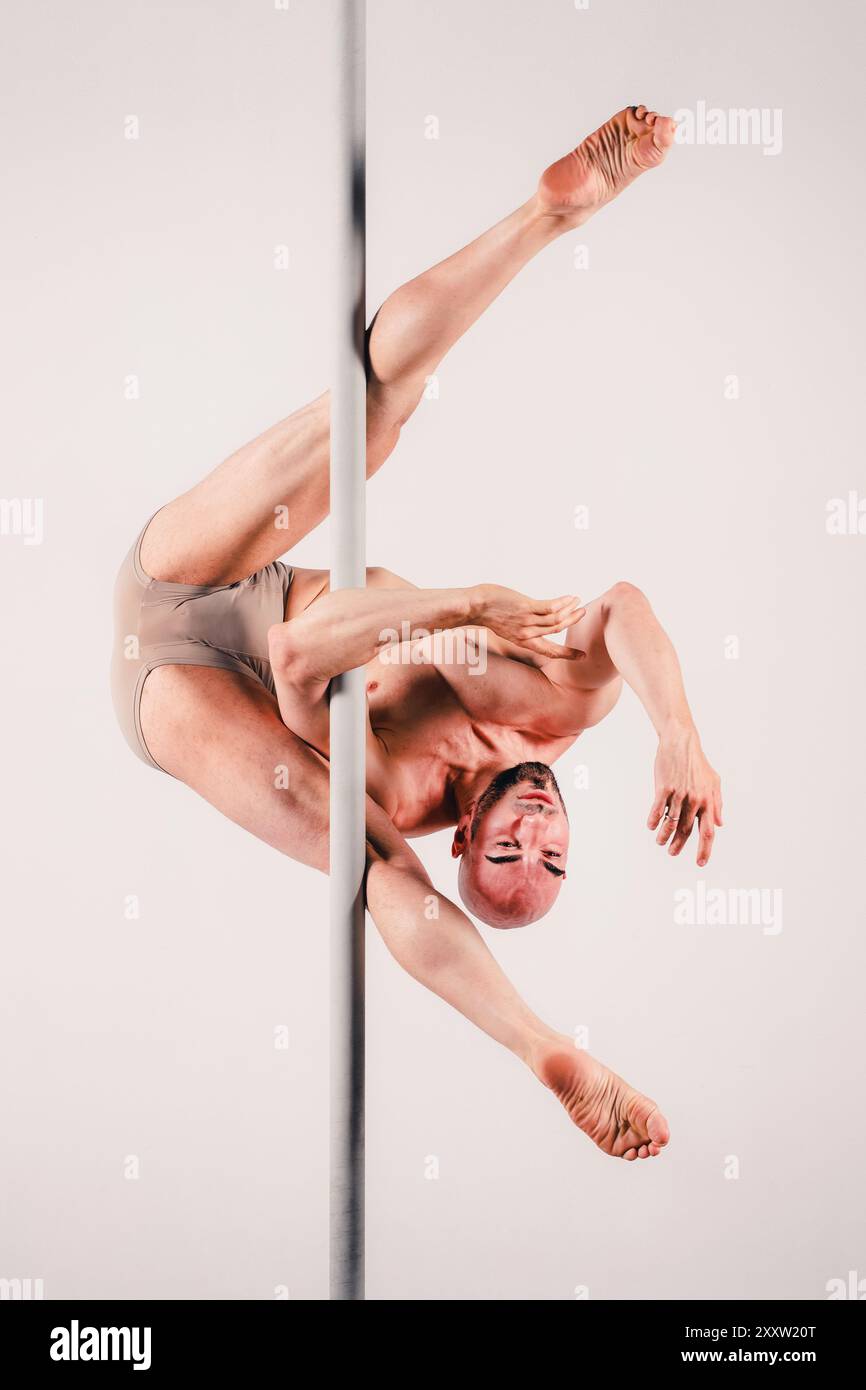 Full length shot of muscular adult man gracefully holding pole performing acrobatics that showcase strength and flexibility in studio Stock Photo