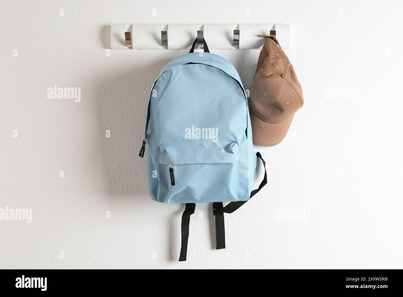 Light blue backpack and cap hanging on white wall Stock Photo