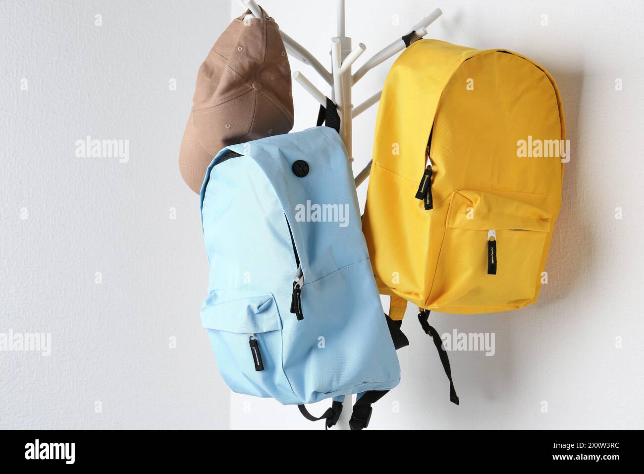 Bright backpacks and cap hanging on white wall Stock Photo