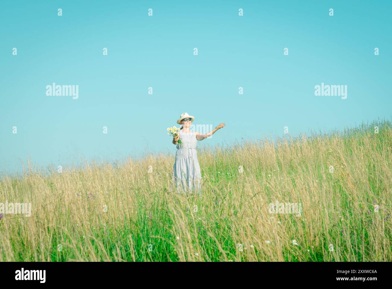 Happy mature woman with wildflowers in a tall grass field on a bright summer day. Stock Photo