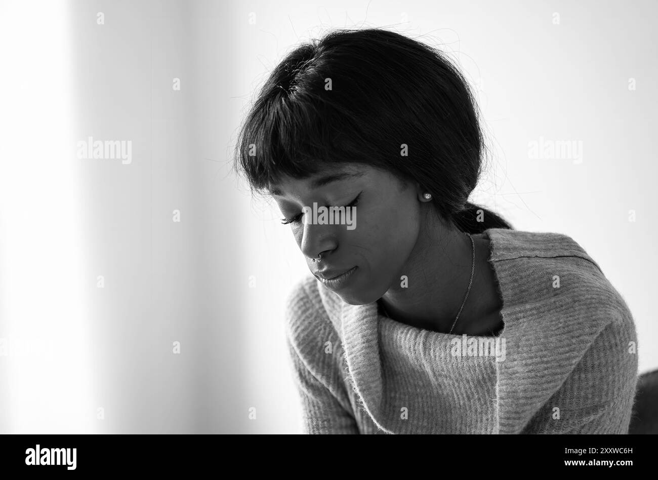 Young black woman in deep thought, captured in a serene black and white portrait. The image emphasizes emotional depth and introspection, highlighting Stock Photo