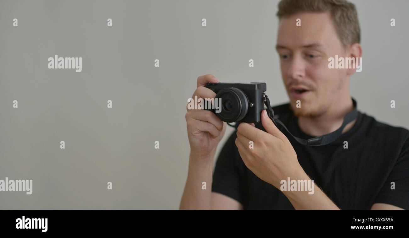 Young man with a photocamera. The photographer looks emotionally at the photo on the camera screen. Professional photographing concept. Design banner Stock Photo