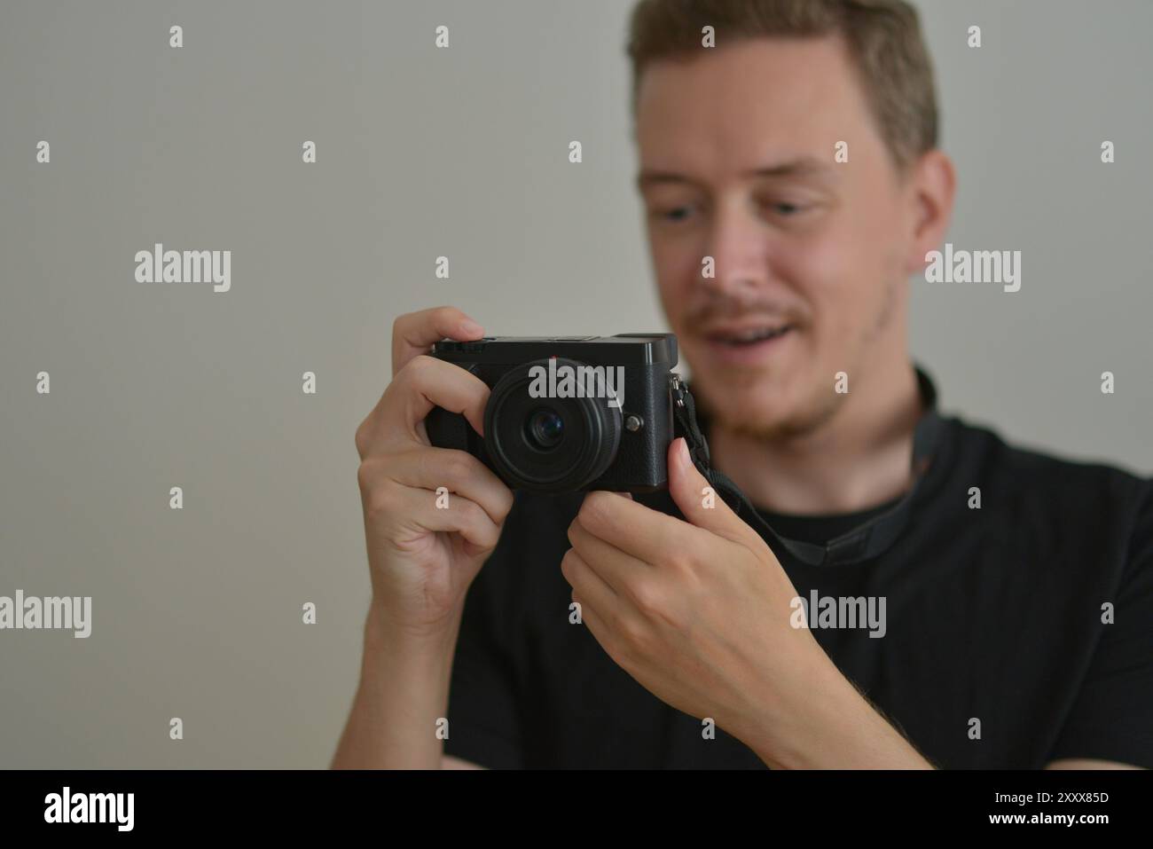 Young man with a photocamera. The photographer looks emotionally at the photo on the camera screen. Professional photographing concept. Stock Photo