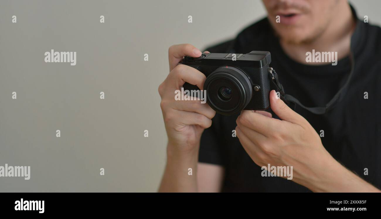 Young man with a photocamera. The photographer looks emotionally at the photo on the camera screen. Professional photographing concept. Design banner Stock Photo