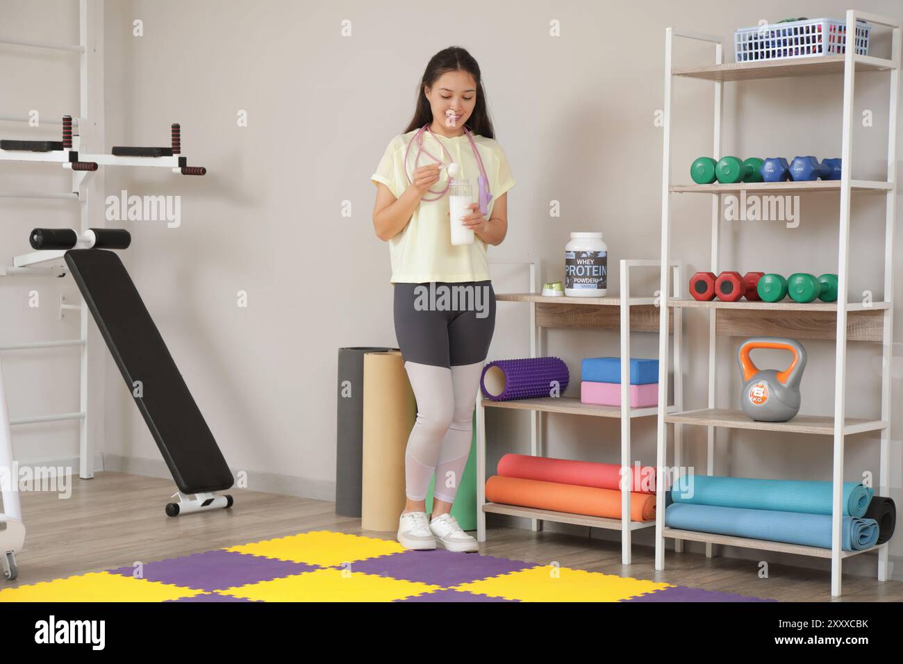 Sporty young happy Asian woman with jumping rope making protein shake ...