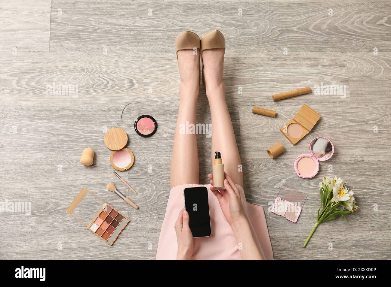Makeup artist with mobile phone and cosmetic products on wooden floor ...
