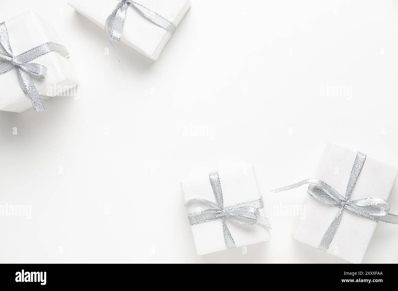 Four white gift boxes with silver ribbons on white background with copy space. Stock Photo
