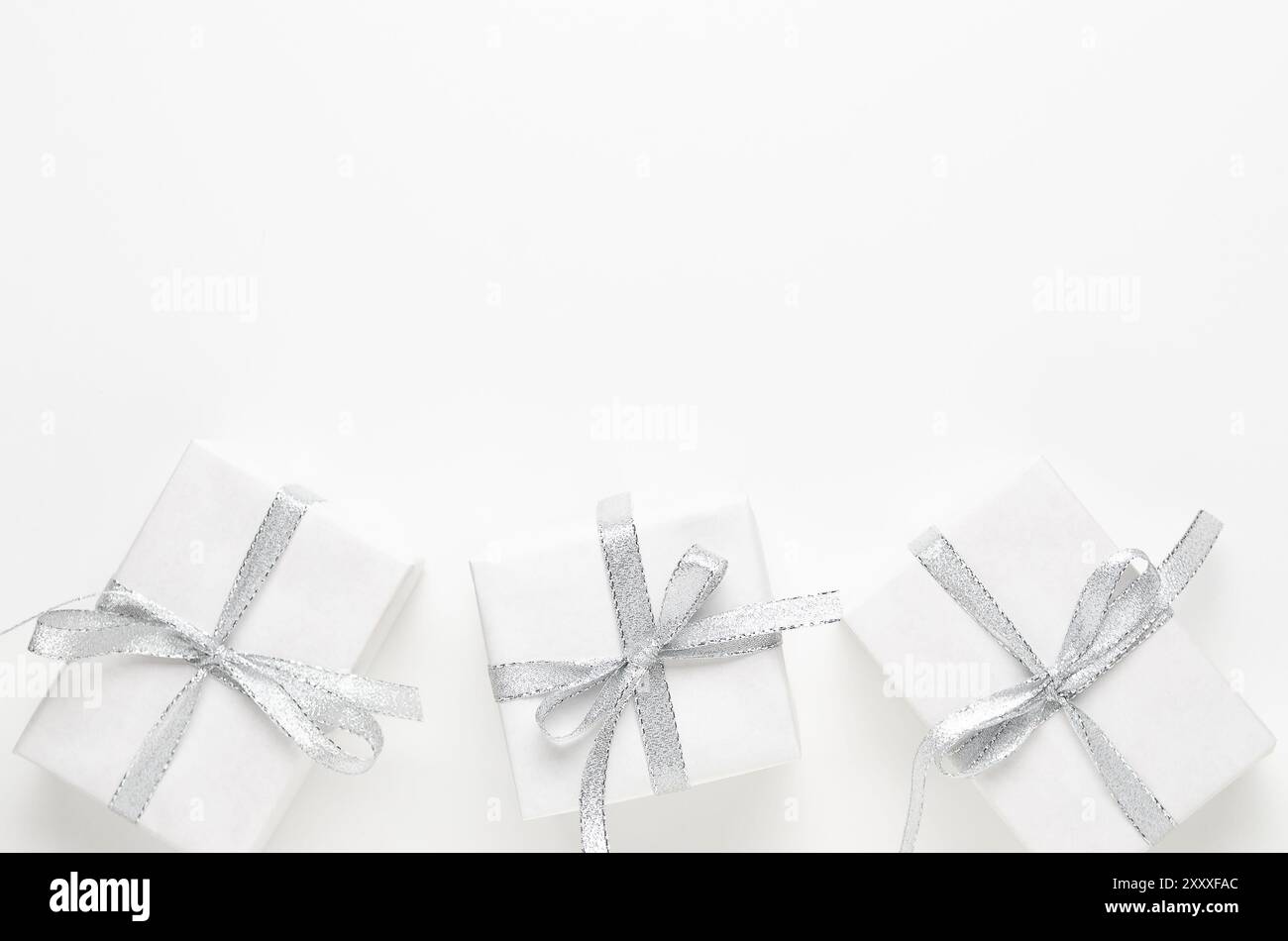 Three white gift boxes with silver ribbons on white background with copy space. Stock Photo