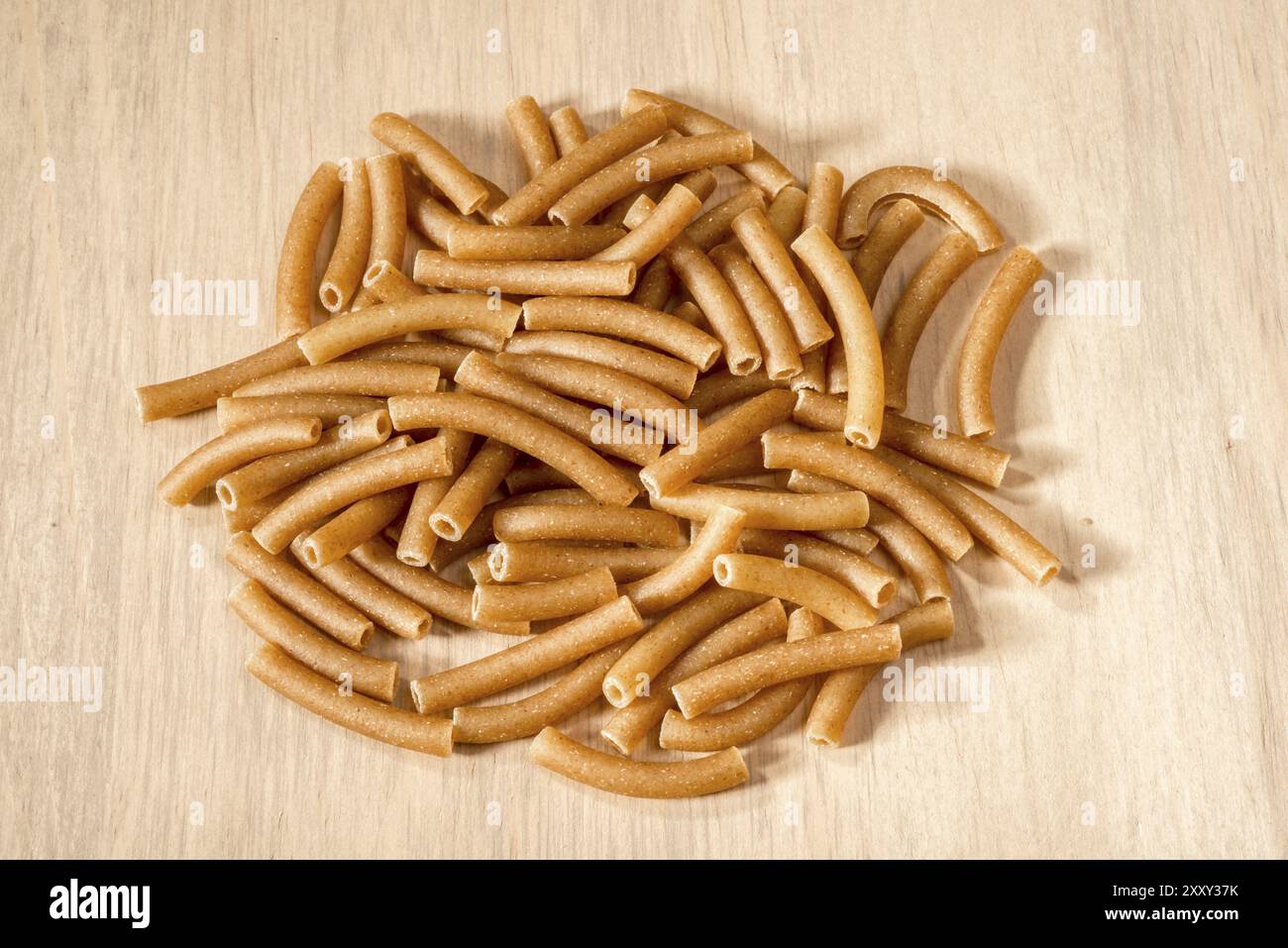 A small heap of wholewheat macaroni pasta on a wooden surface Stock Photo