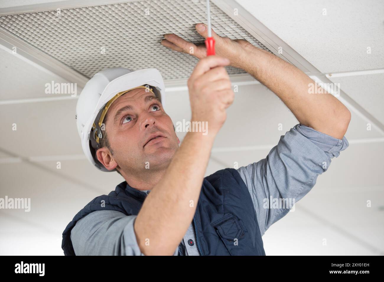 workman securing screws on ceiling vent Stock Photo