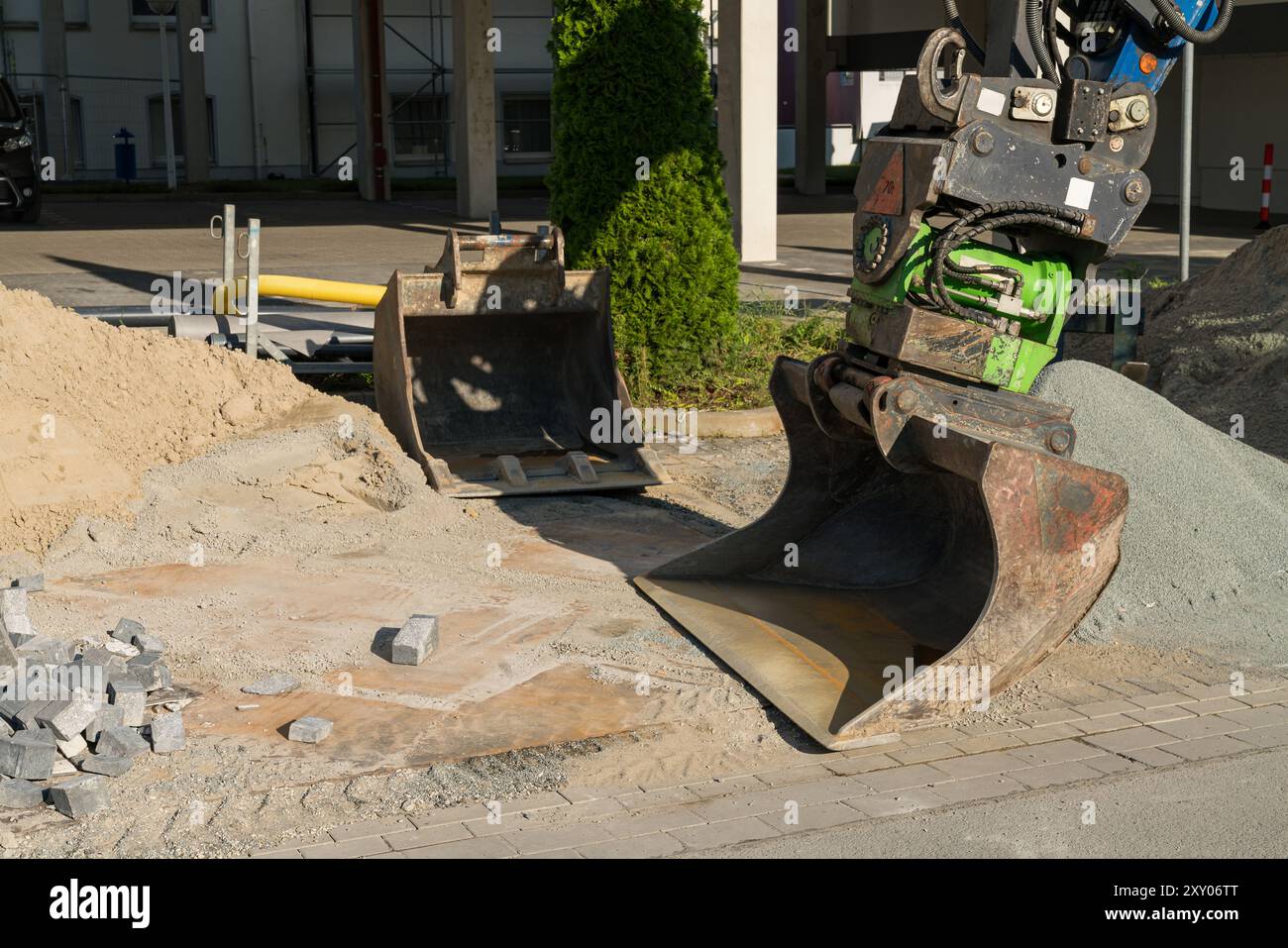 A large construction machine is positioned on a work site, ready to dig and transport gravel and sand, with construction materials scattered around. Stock Photo