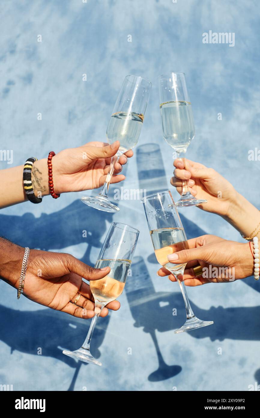 Four hands are holding champagne glasses for a toast against a blue ...