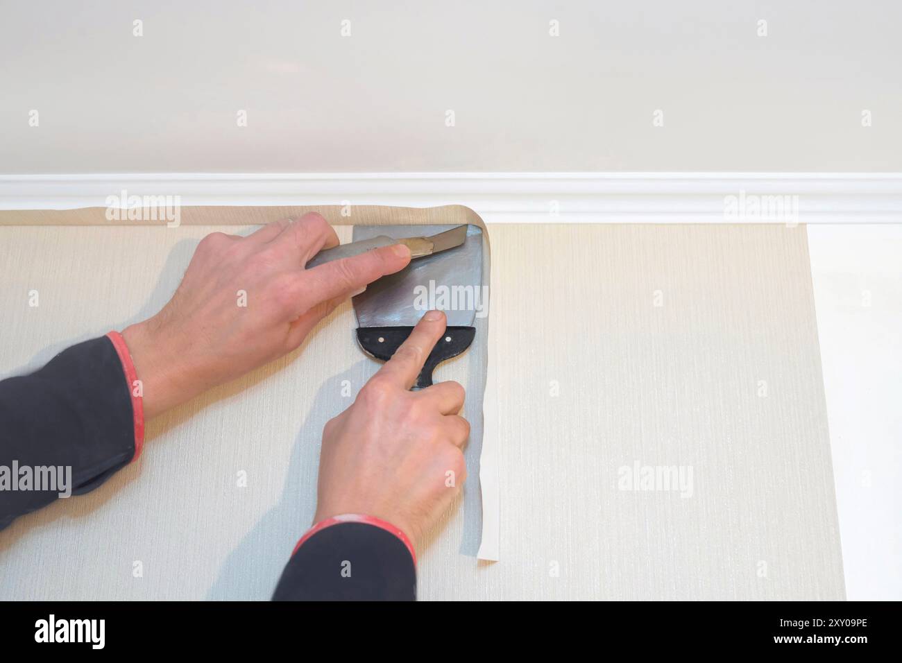 A worker cuts the wallpaper with a spatula and an office knife. Repair concept Stock Photo