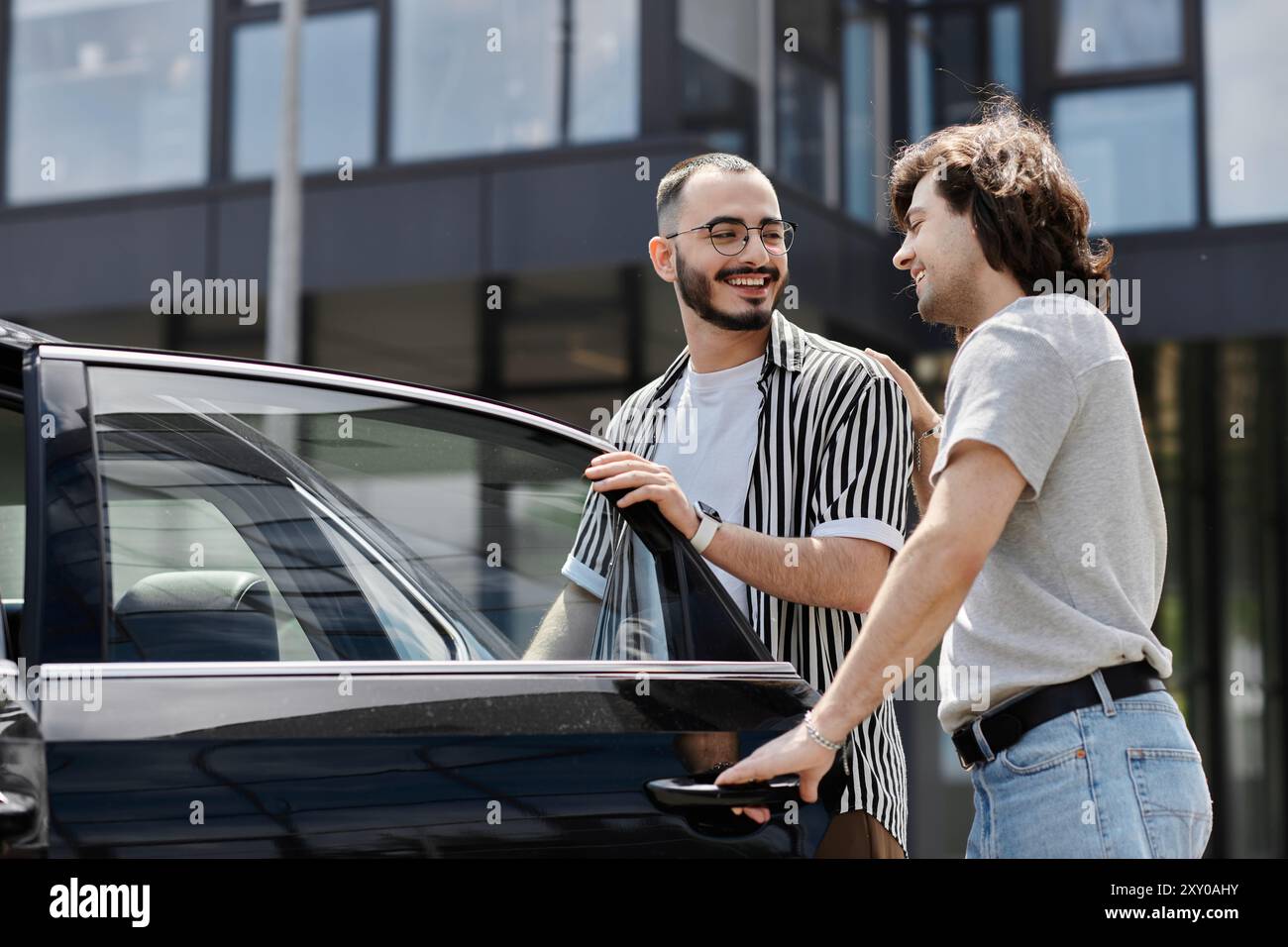 Two men stand beside a car, smiling and laughing together Stock Photo ...