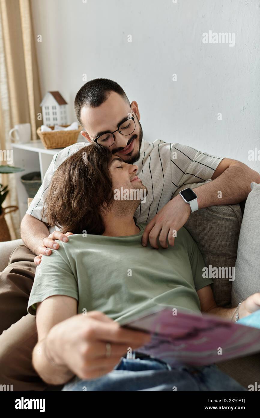 A gay couple lounges on a couch, one reading as the other rests his ...