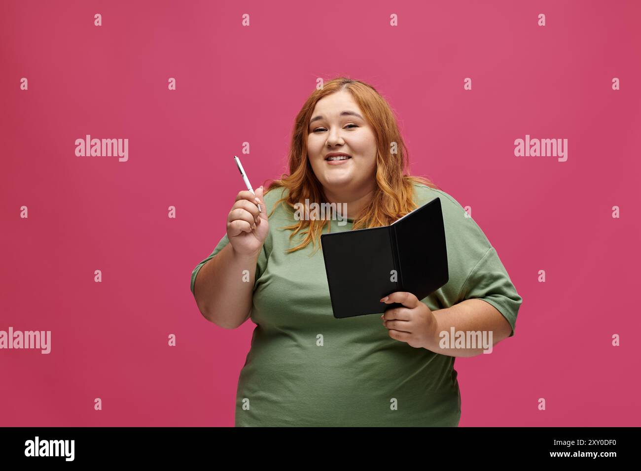 A woman smiles confidently while holding a pen and notebook. Stock Photo