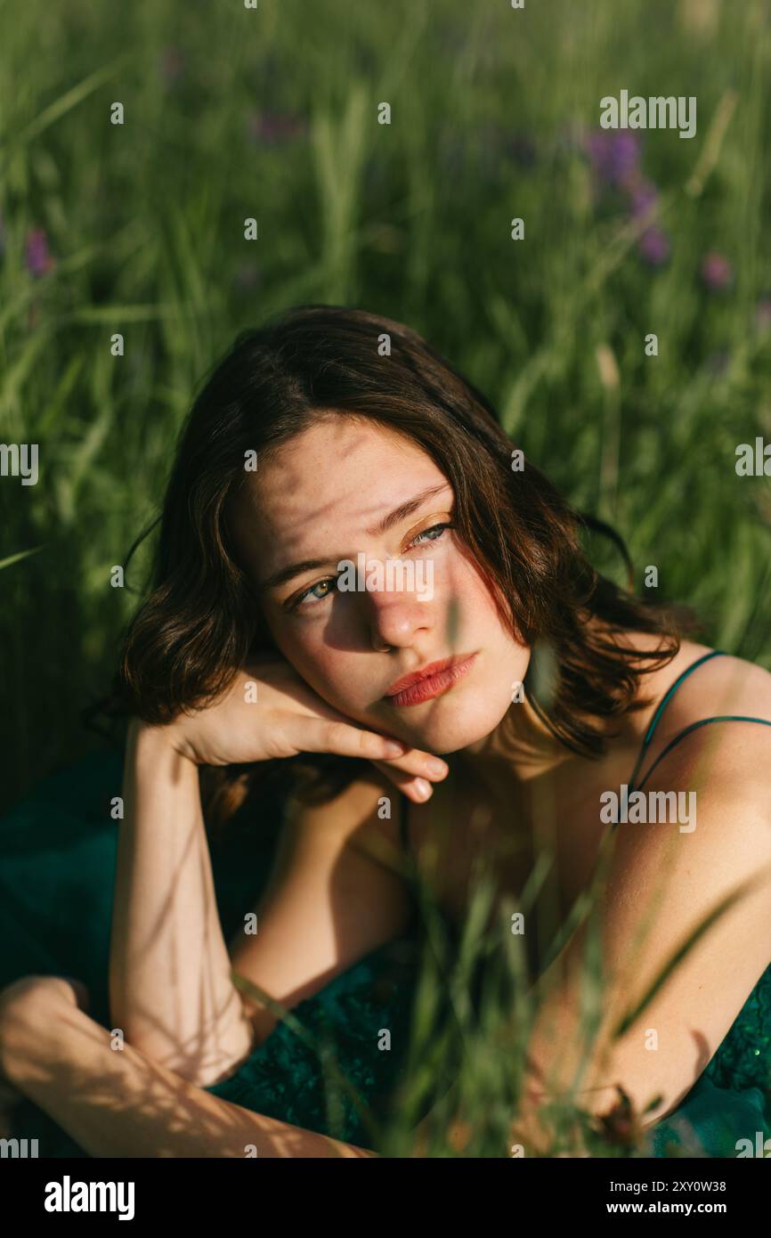 A teenage girl wearing a shimmering green prom dress poses thoughtfully ...