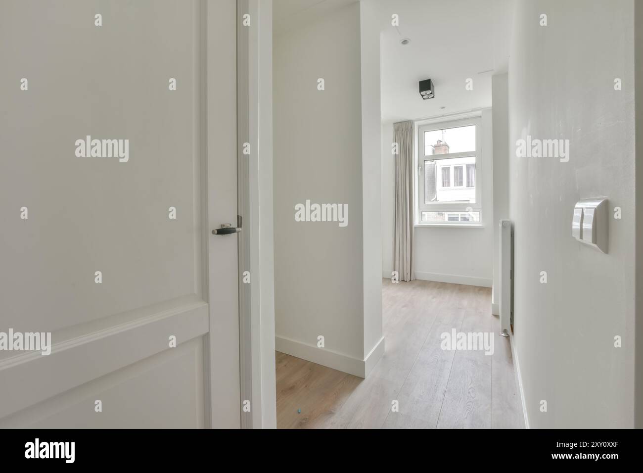 A bright, contemporary hallway in a modern home, well-lit with natural sunlight streaming through a window. Stock Photo