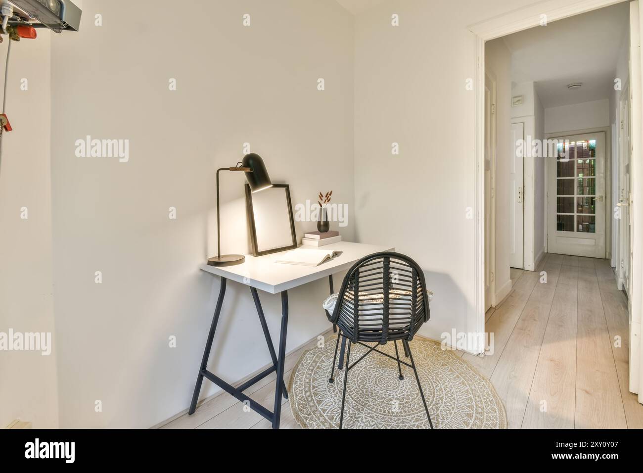 A cozy and minimalist home office corner with a sleek white desk, modern black chair, lamp, decorative vase, and empty picture frame, illuminated by n Stock Photo