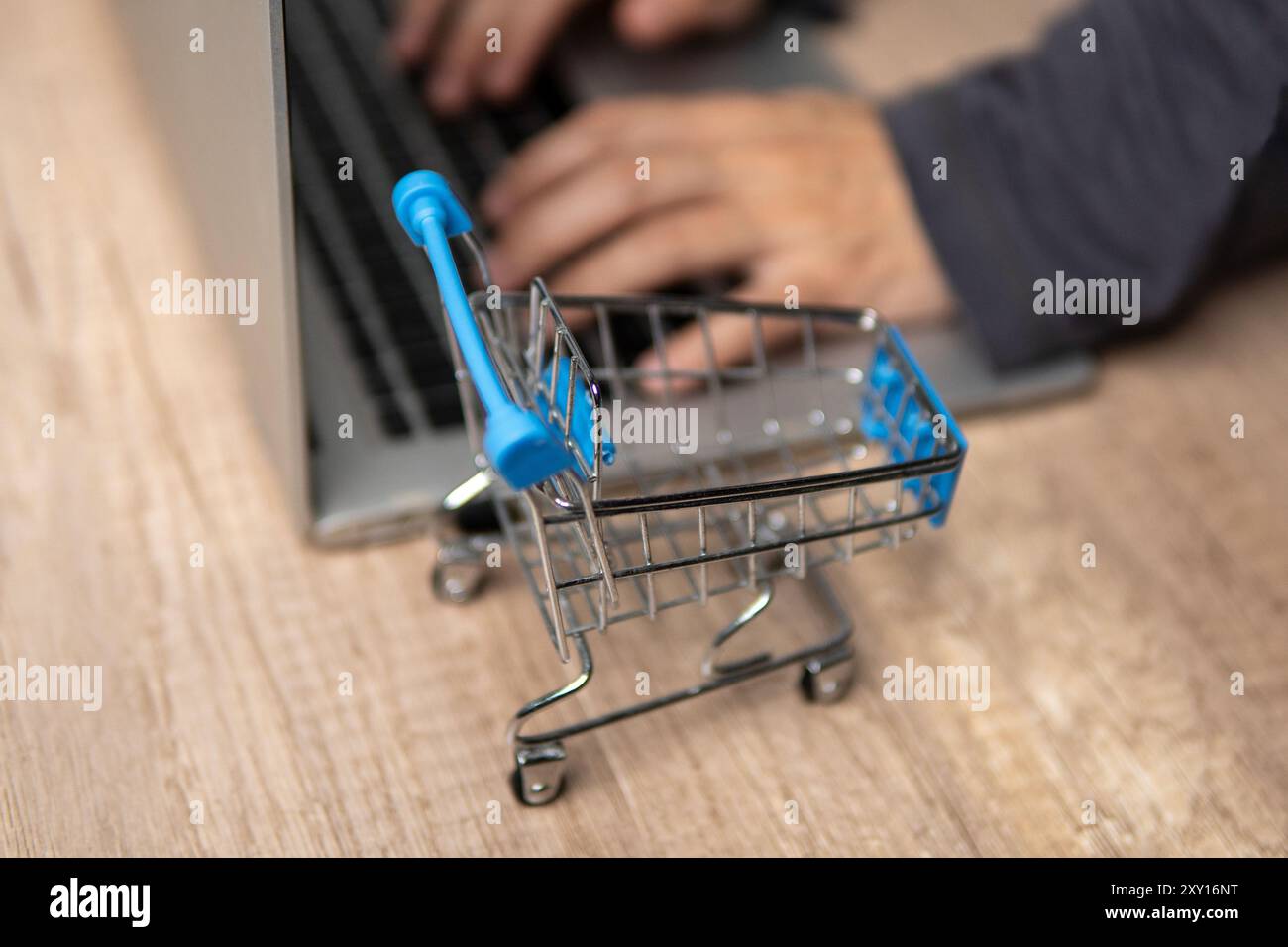 Close-up of mini shopping trolley and hands typing on laptop. Online shopping concept. Stock Photo