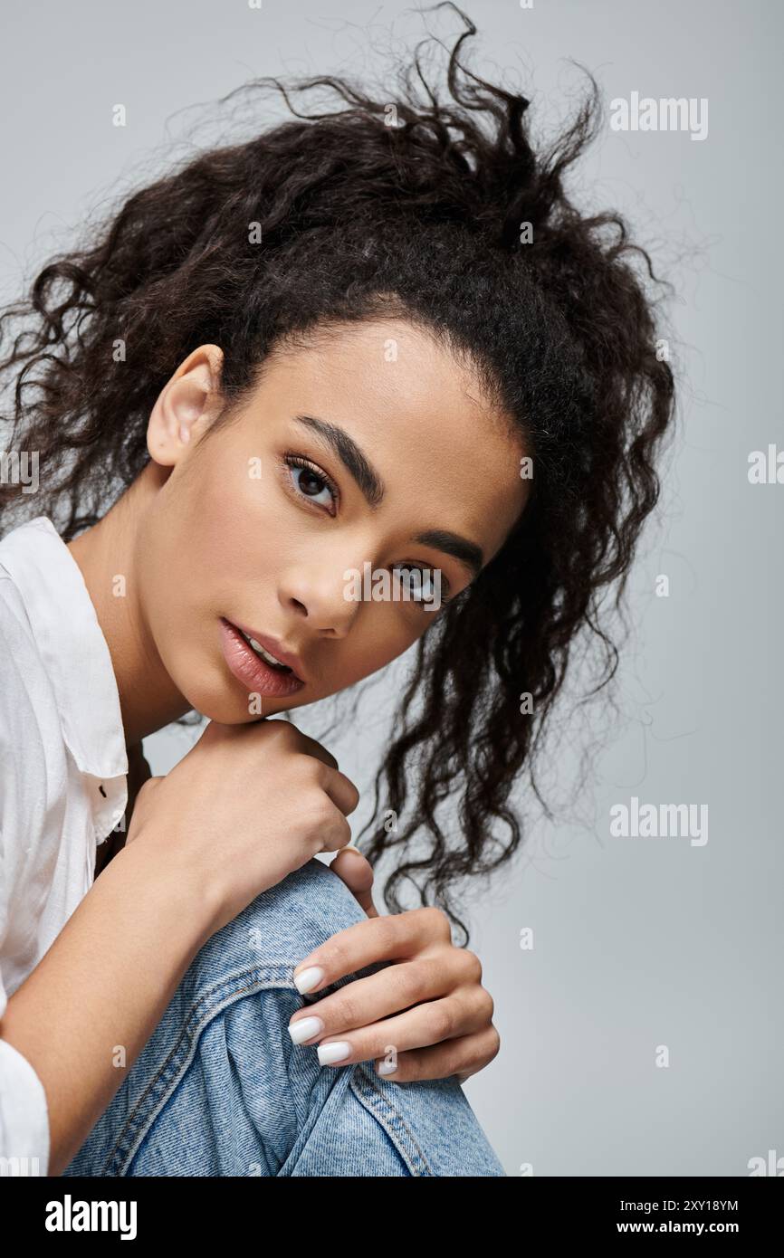 A young Black woman with curly hair poses against a grey background ...
