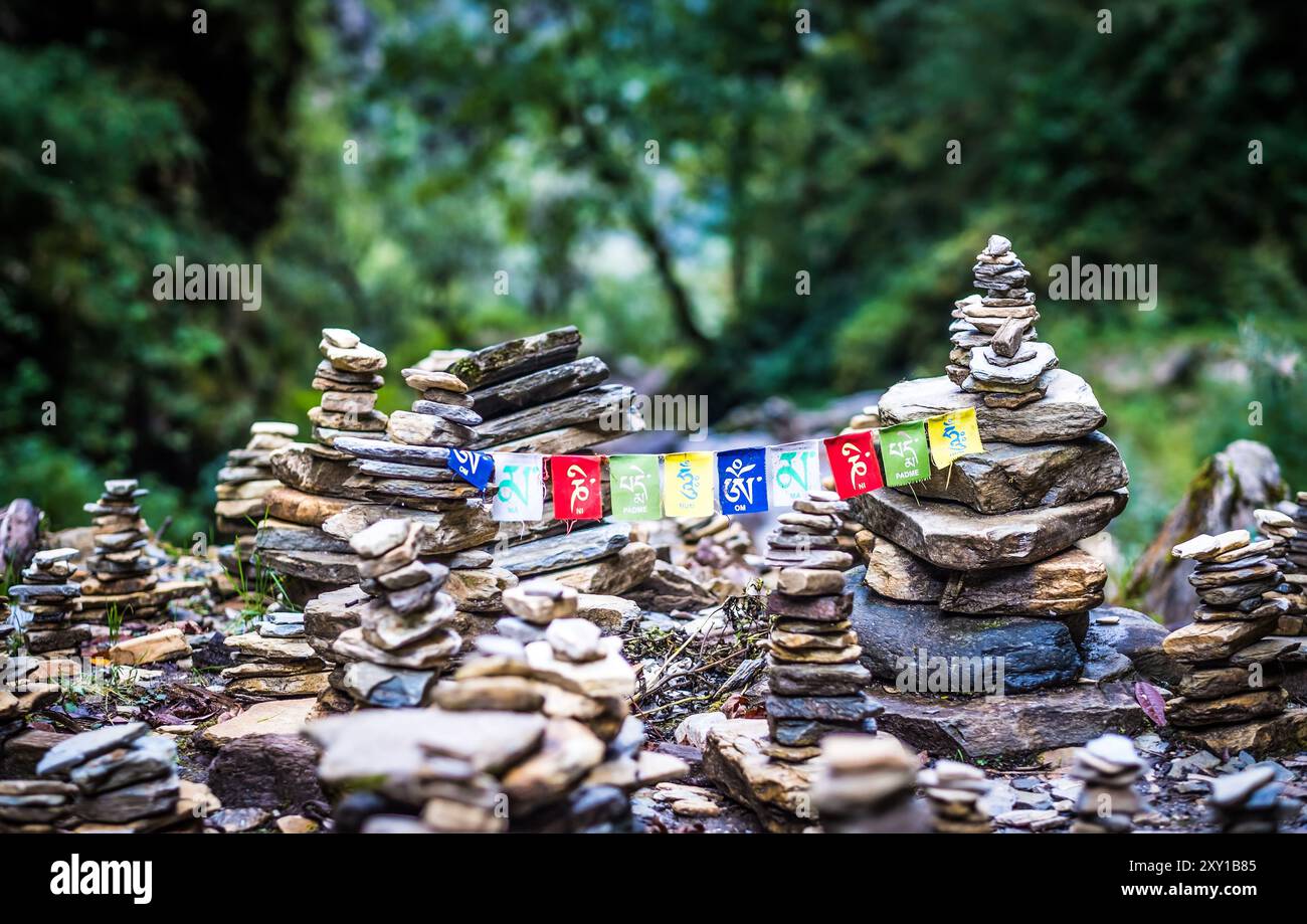 Sanskrit calligraphy of Buddhist Mantra Om Mani Padme Hum on multicolored flags hanging between two meditation stone pile on Annapurna track. Stock Photo