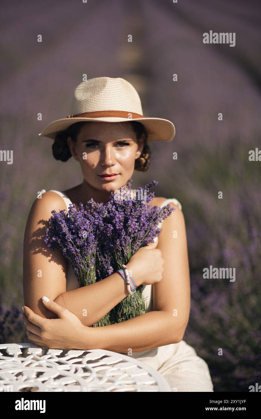 woman sitting in a field of lavender and wearing a straw hat. She is ...