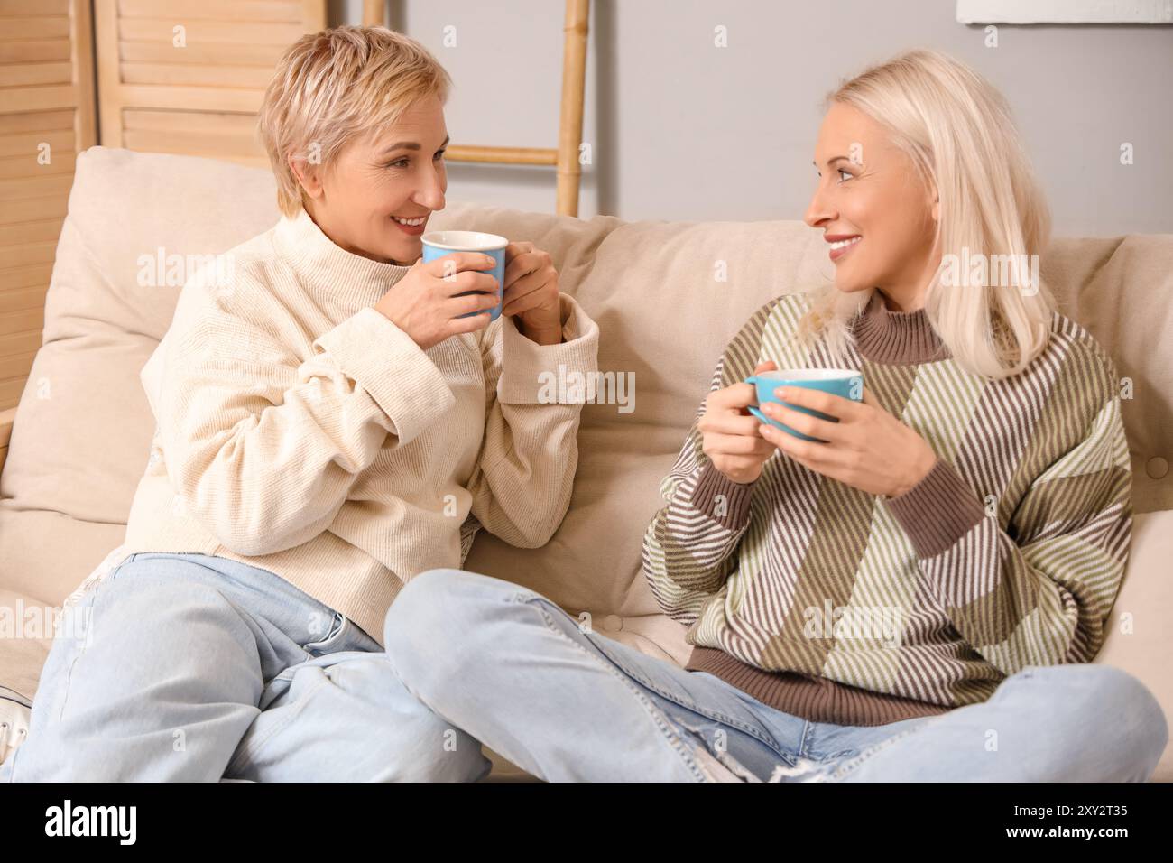 Mature women with cups of tea sitting on sofa at home Stock Photo - Alamy