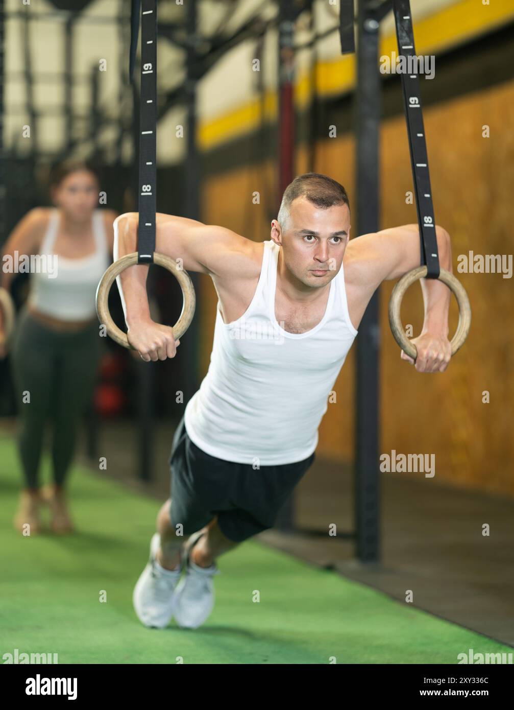 Sportive young guy working out with gymnastic rings in gym during