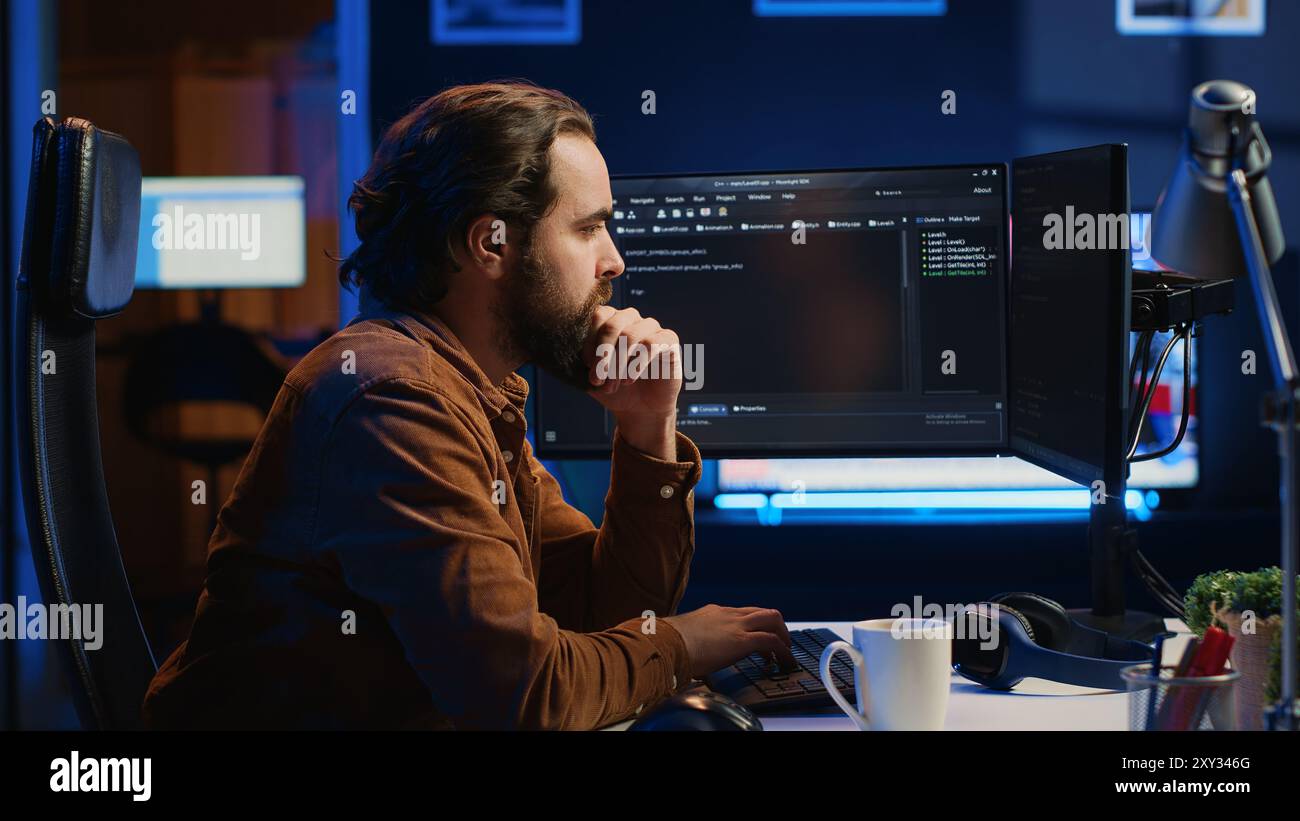 Programmer doing web development during remote job shift in neon lit home office, finishing coding project. IT specialist sitting at computer desk, working on desktop PC, camera A Stock Photo