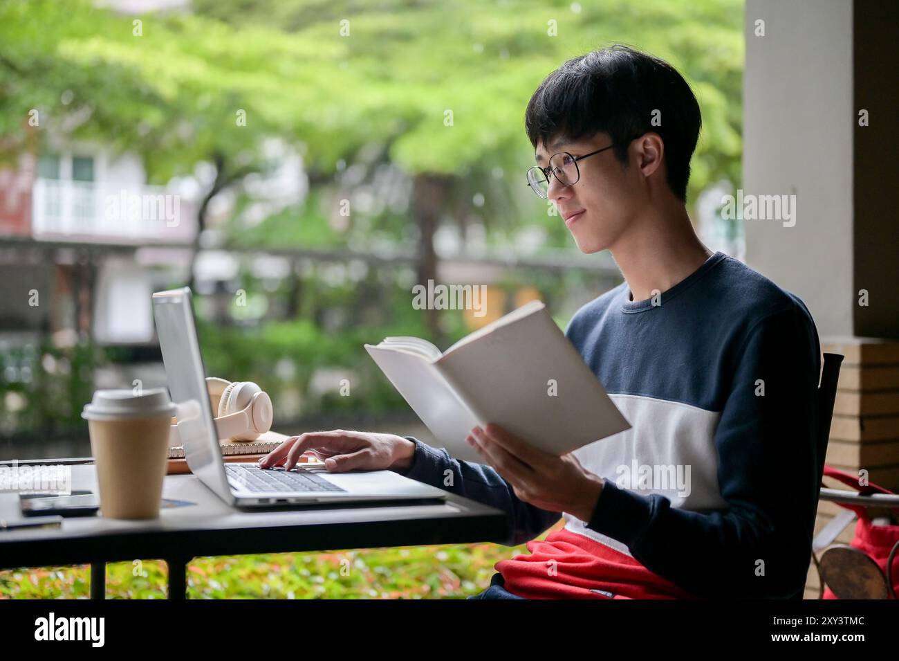 A young, positive Asian male college student wearing glasses is working ...