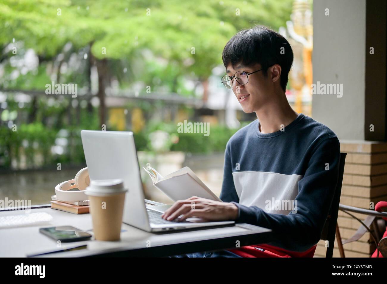 A young, positive Asian male college student wearing glasses is working ...