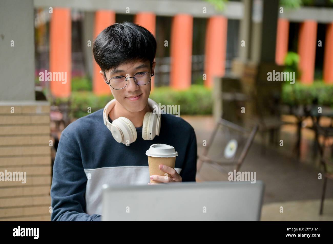 A young, positive Asian male college student wearing glasses is working ...
