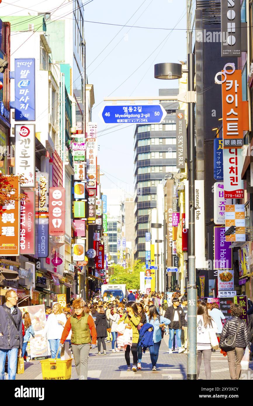 Seoul, South Korea, April 17, 2015: Tourists walking down bustling Myeongdong pedestrian shopping street surrounded by commercialism of stores, signs Stock Photo