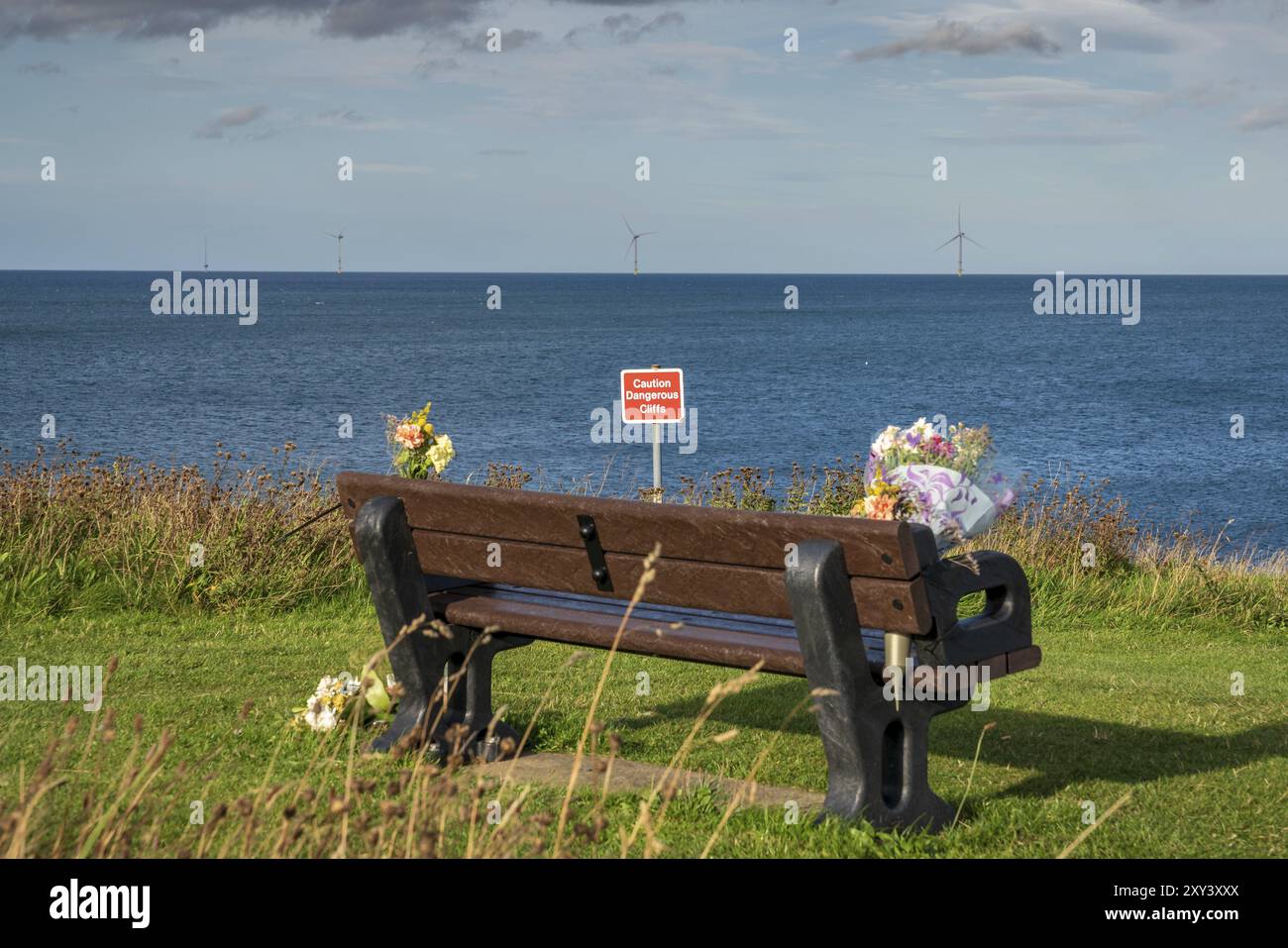 A bench with flowers, seen at North Sea coast in Collywell Bay, Seaton Sluice in Northumberland, England, UK Stock Photo