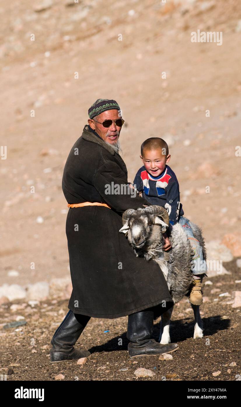 A Kazakh Grandfather helping his grandson ride a big goat. Photo taken ...