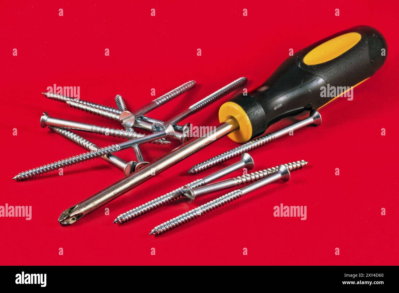 Screw driver and screws against a red background Stock Photo
