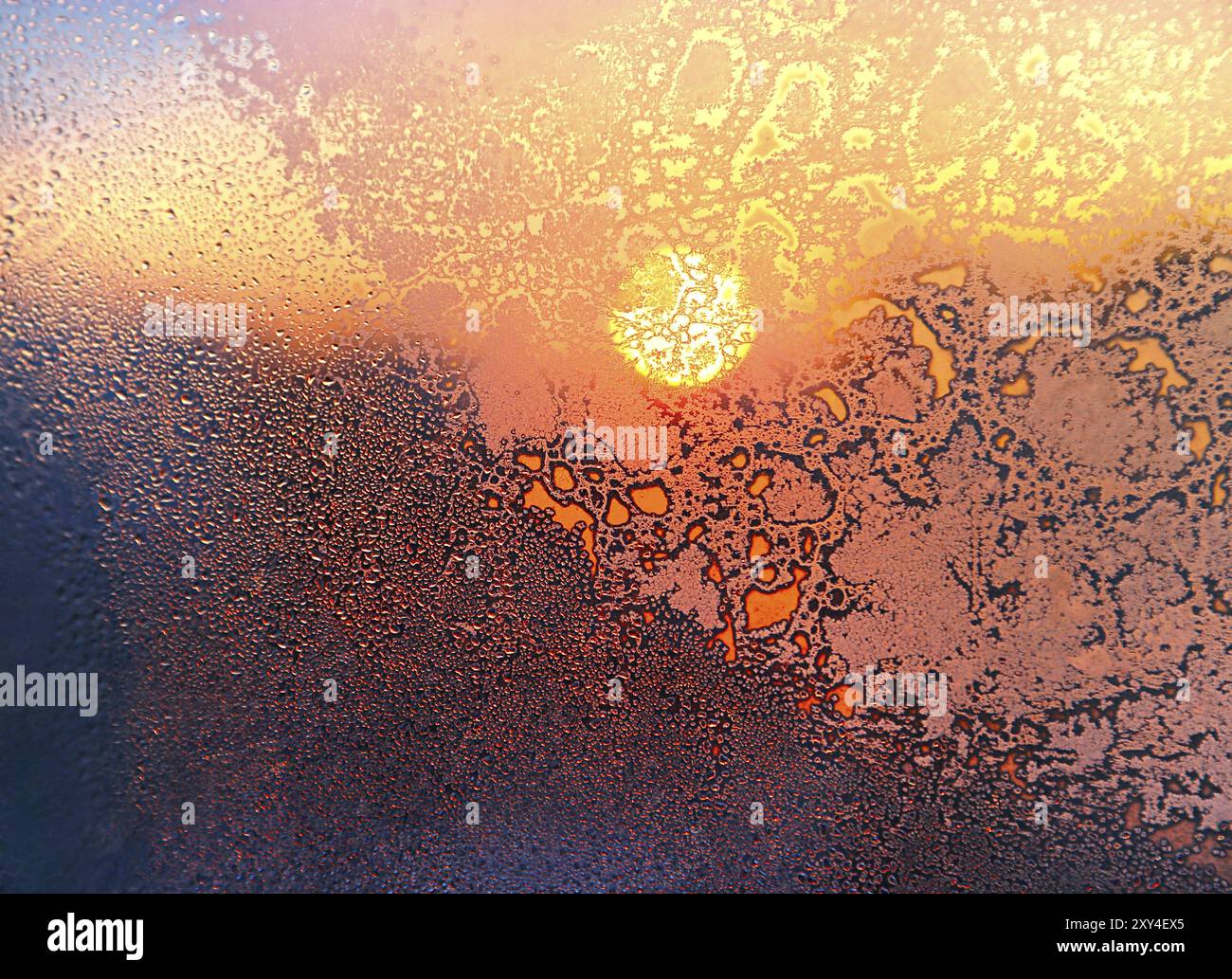 Nature background with ice pattern, bright sunlight and water drops on winter window glass Stock Photo