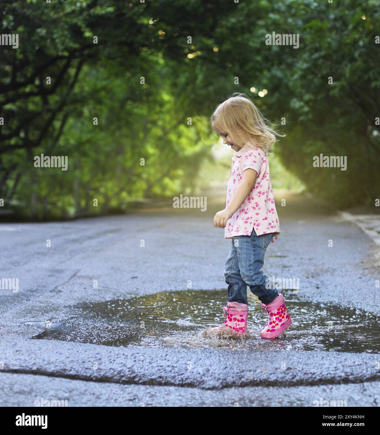 Cute little girl wearing rain boots jumping into a puddle Stock Photo ...