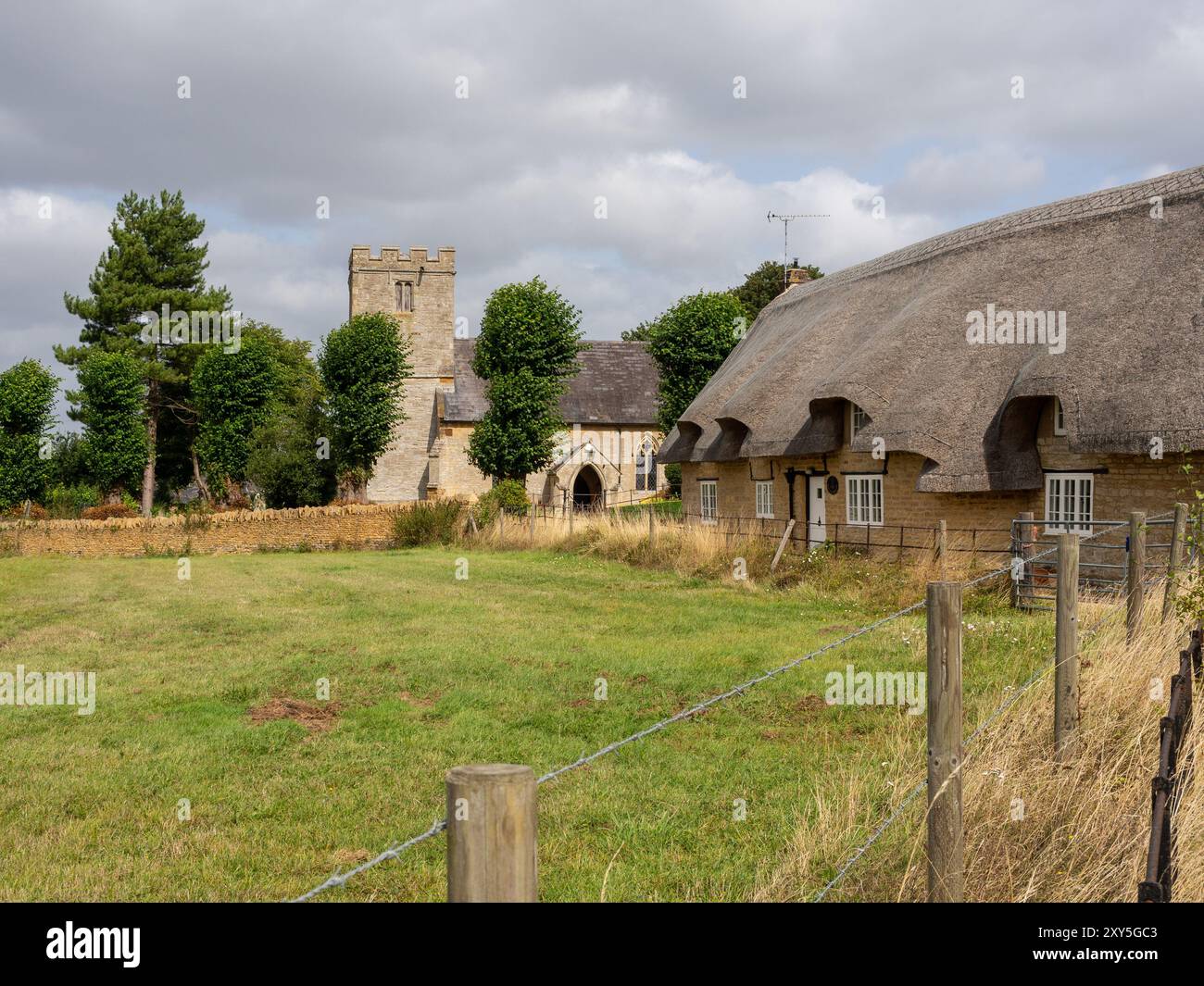 Thatched house with a church in the background, a quintessential English scene from the village of Alderton, Northamptonshire, UK Stock Photo